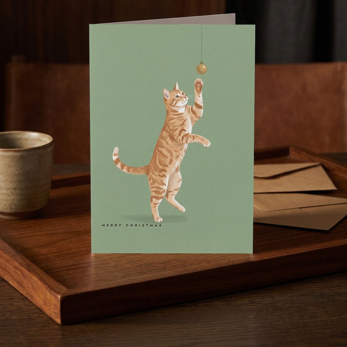 A folded card standing on a dark teak tray beside a small stoneware cup
