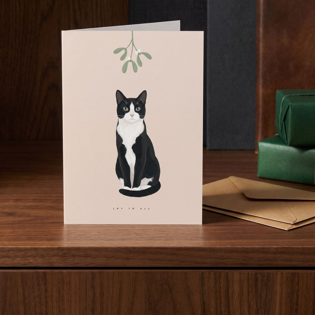 A folded card standing on a walnut sideboard beside two presents wrapped in green
