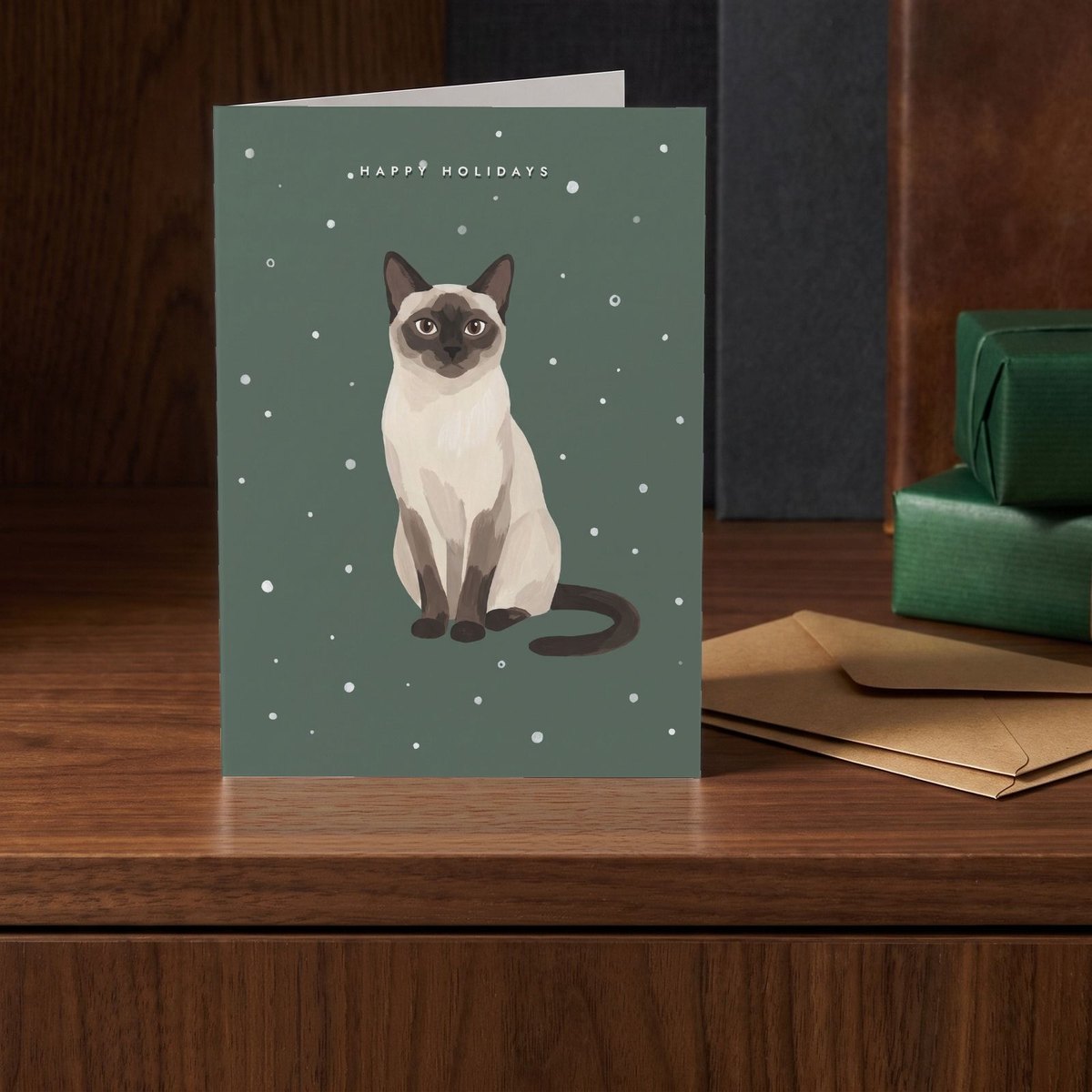 A folded card standing on a walnut sideboard beside two presents wrapped in green