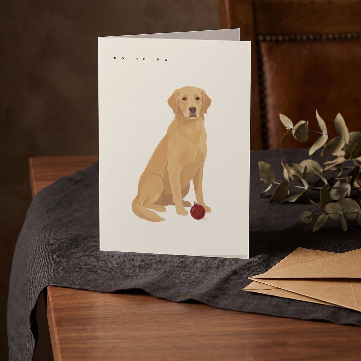A folded card standing on a charcoal linen cloth with a sprig of dried eucalyptus